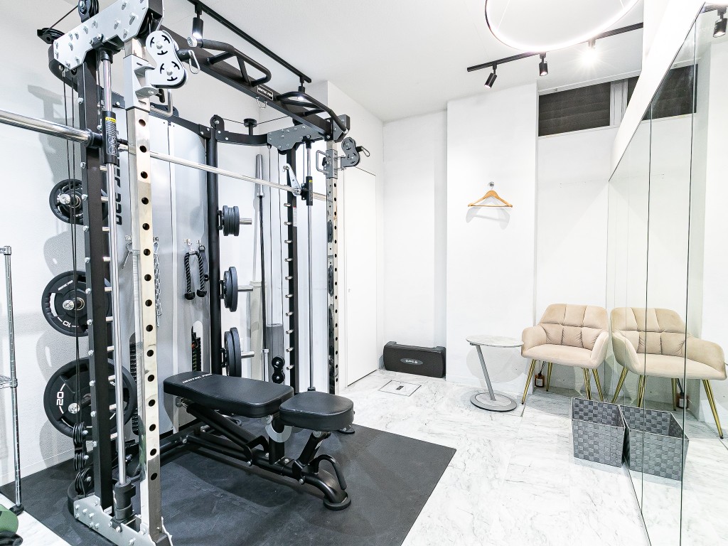 パワーラックやベンチを備えた明るいパーソナルトレーニングスタジオの内観。